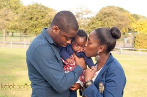 Mum and dad kiss baby in the park.