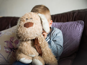 Boy covering face with teddy bear