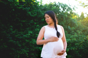 Pregnant woman with hand on bump in outdoor maternity photo shoot.