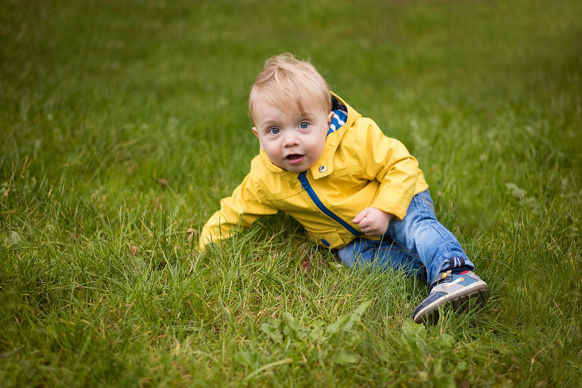 Toddler seating on green grass in outdoor location.