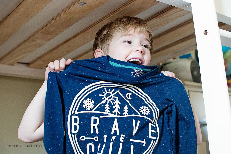 Little boy holding his 'brave in the chill' t-shirt